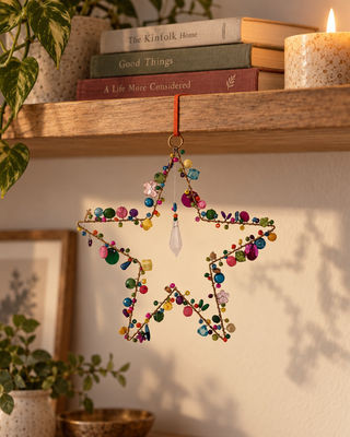 Perlen Stern pink bunt an einer Regalkante mit Büchern und Kerze