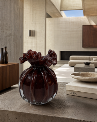 Glasvase Bordeaux, kleine rote Vase mit Blütenrand, auf einem Tisch im hellen Wohnzimmer mit Meerblick